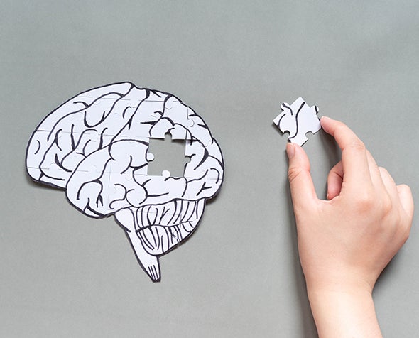 A cutout of a brain is shown with a puzzle piece missing and is in a hand.