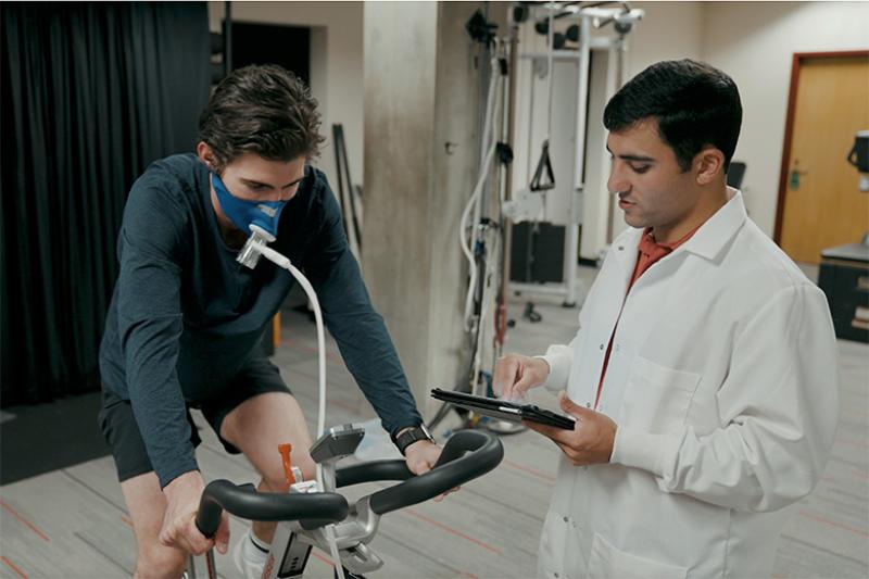 A student conducts physiology research with an athlete using a bicycle