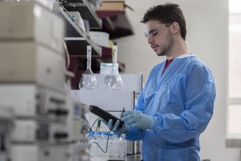 A student in a lab gown in a lab with vials on the table